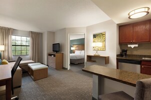 Ein Hotelzimmer mit Bett, Schreibtisch, Fernseher, einer Küchenzeile und einem Fenster mit Vorhängen.