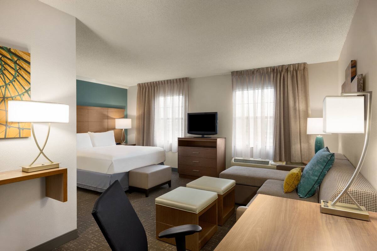 Une chambre d’hôtel comprenant un lit, un bureau, une télévision et un coin salon avec des coussins.