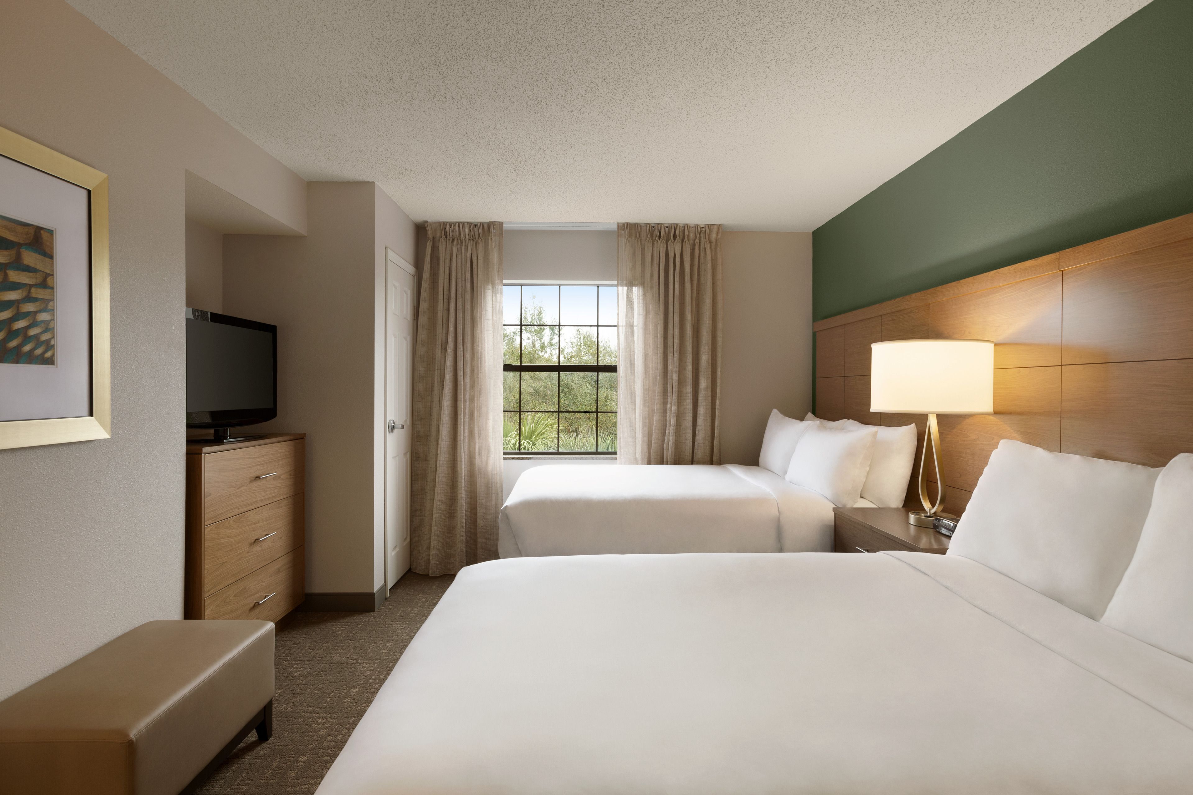 A hotel room with two beds, a TV, a desk, and a window with curtains.