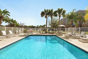 Une piscine entourée de chaises longues blanches et de palmiers en arrière-plan.