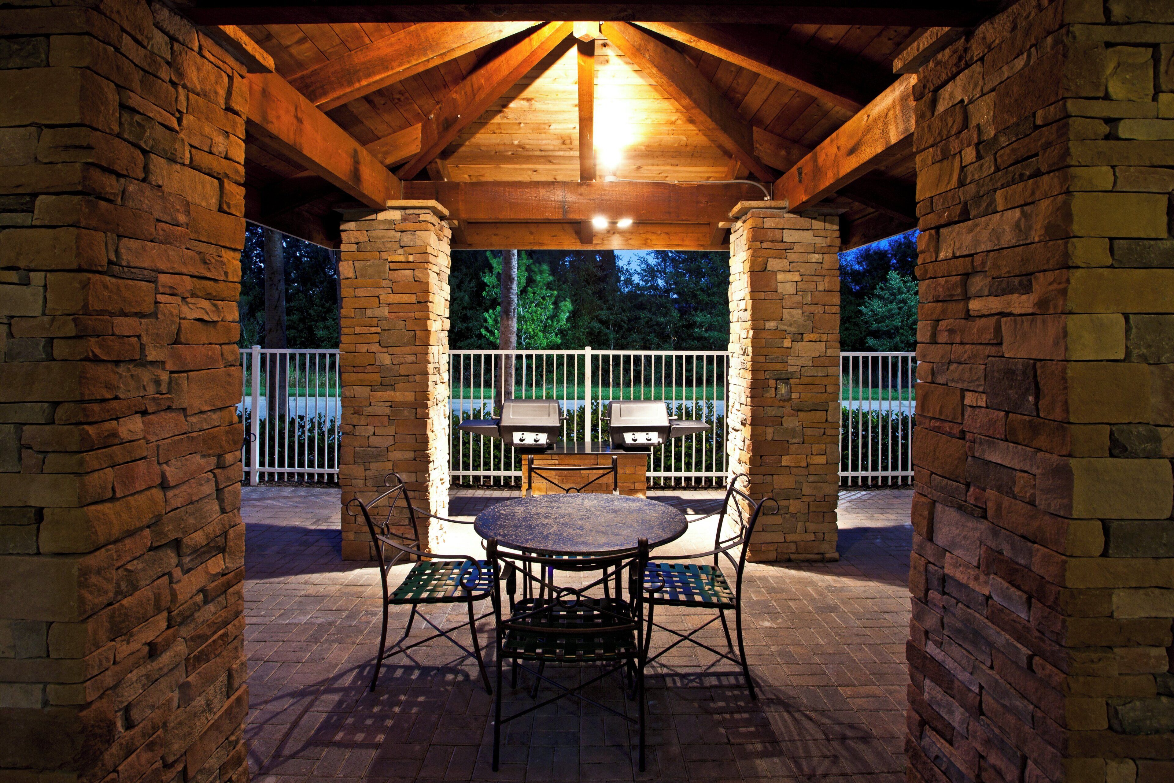 Un patio al aire libre con pared de ladrillo, techo de madera y una mesa con sillas.