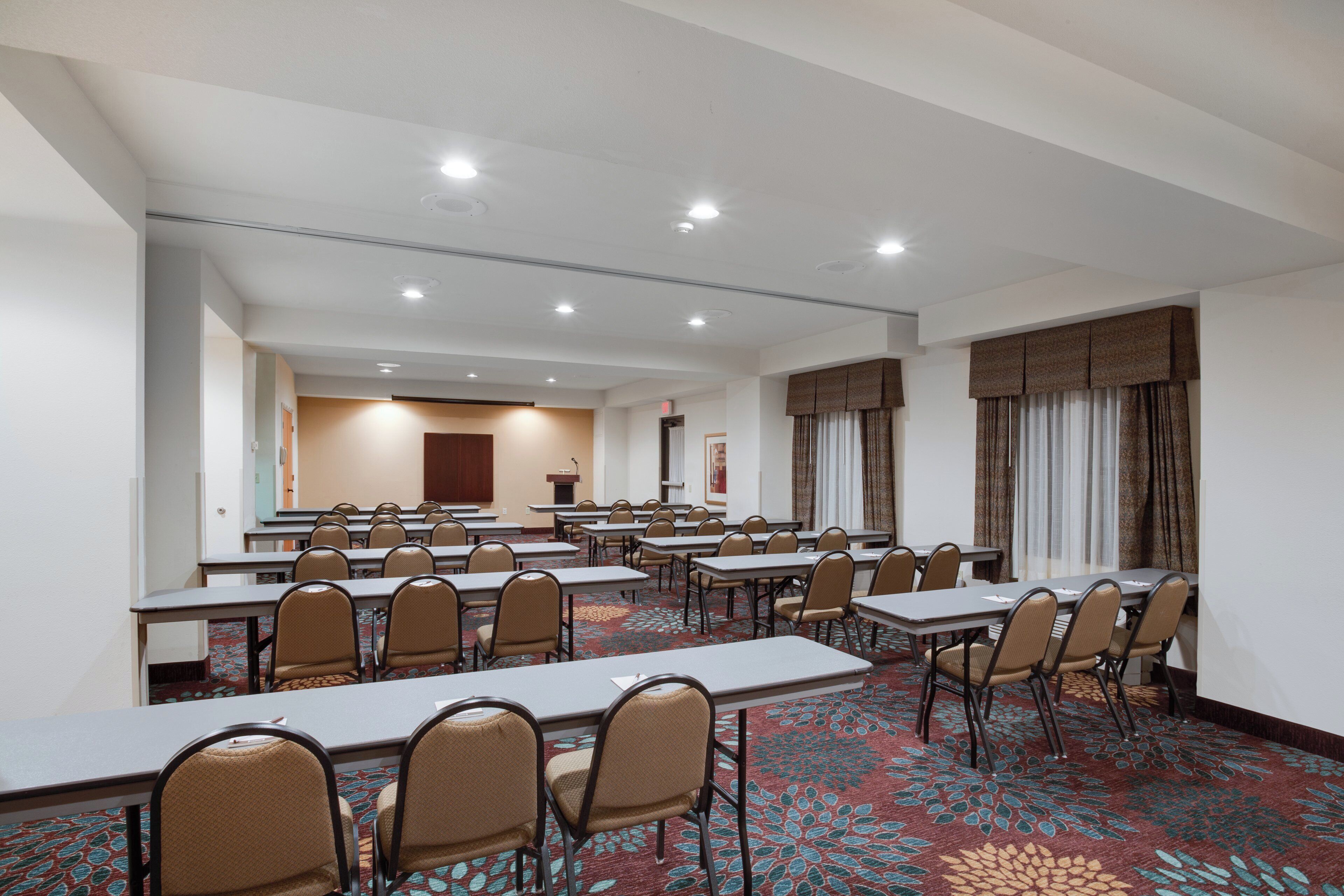 A conference room with multiple tables and chairs, a podium, and a carpeted floor.