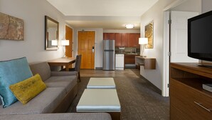 Un espacio habitable compacto con sofá, una mesa de centro, televisor y una kitchenette al fondo.