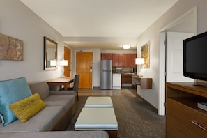 A compact living space with a sofa, a coffee table, a TV, and a kitchenette in the background.