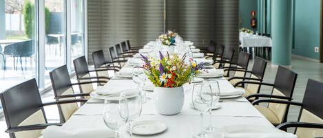 Una larga mesa de comedor con manteles blancos, platos y vasos, y un centro de mesa floral.