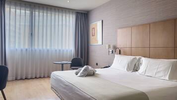 Une chambre d’hôtel avec un grand lit, une petite table, une chaise, une lampe fixée au mur et une fenêtre avec des rideaux.