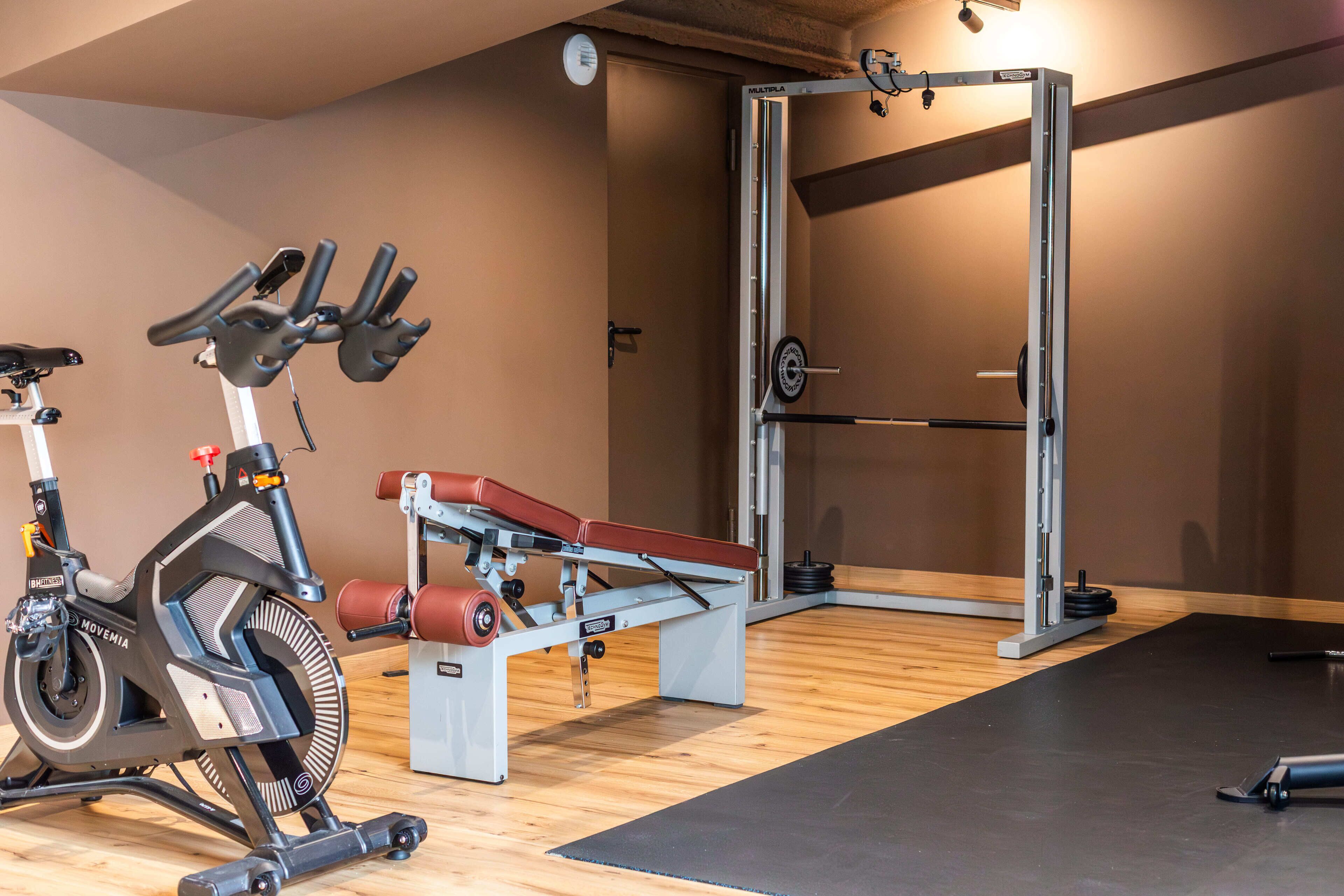 A gym with exercise equipment including a stationary bike, a bench press, and a squat rack.