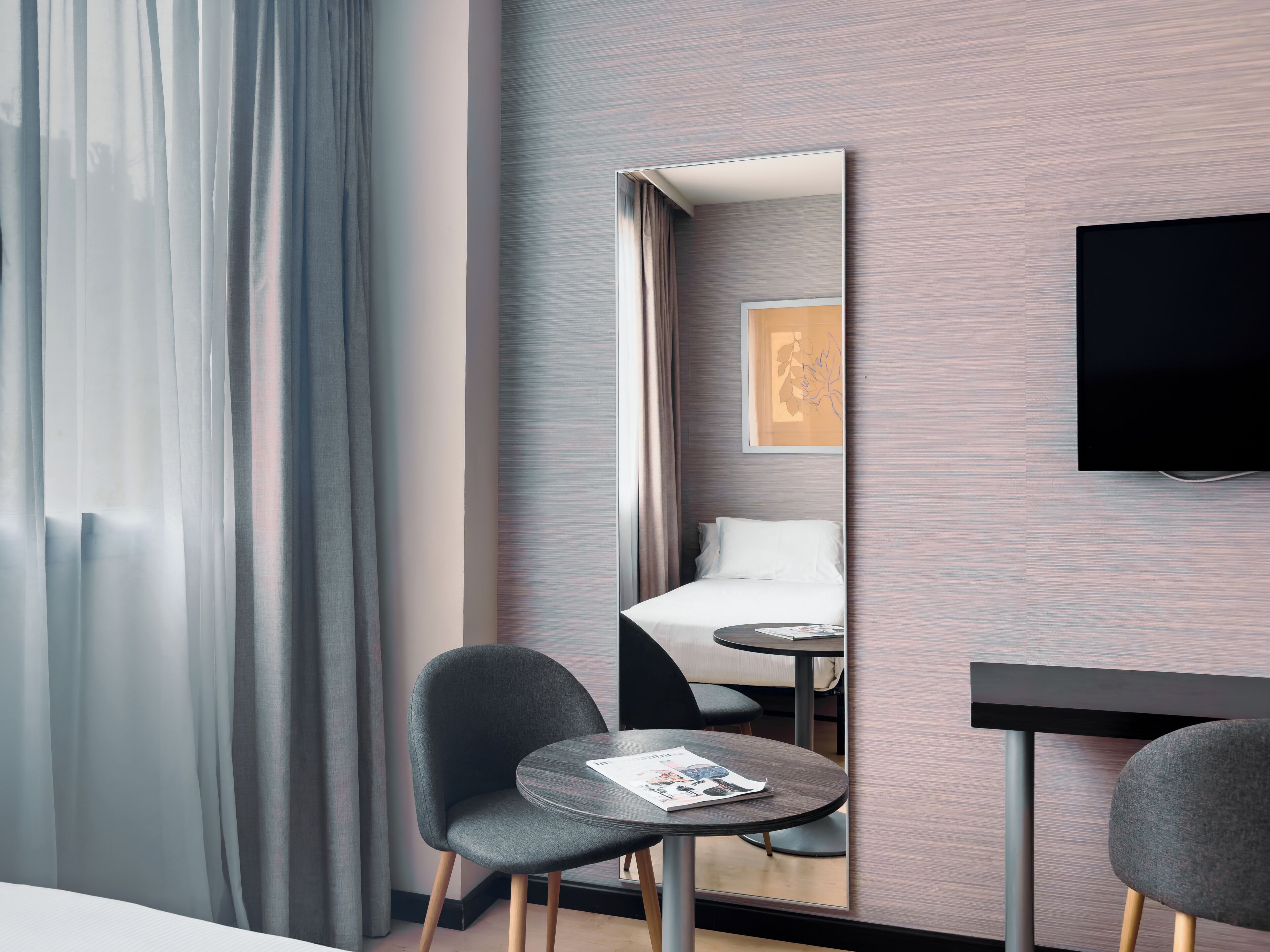 Una habitación de hotel con cama, televisión, una mesita con una revista y una silla.