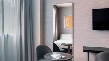 Una habitación de hotel con cama, televisión, una mesita con una revista y una silla.