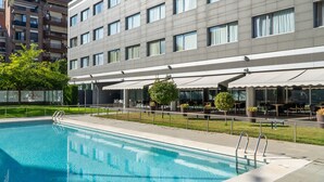 A modern hotel with a swimming pool, outdoor seating, and a view of the cityscape.