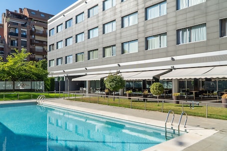 A modern hotel with a swimming pool, outdoor seating, and a view of the cityscape.