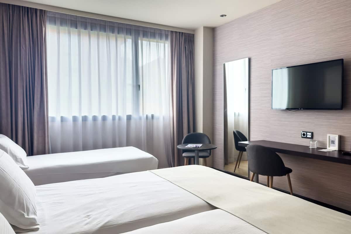 Habitación de hotel con dos camas, un escritorio, una silla, un televisor y una ventana con cortinas.