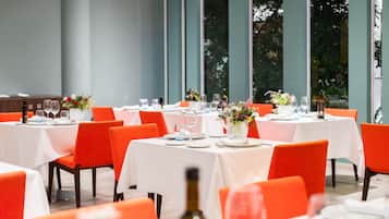 Un comedor con mesas dispuestas para una comida, con manteles blancos y sillas anaranjadas.