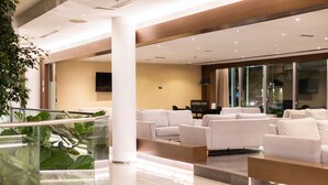 A modern lobby with a glass railing, white sofas, and a flat-screen TV on the wall.