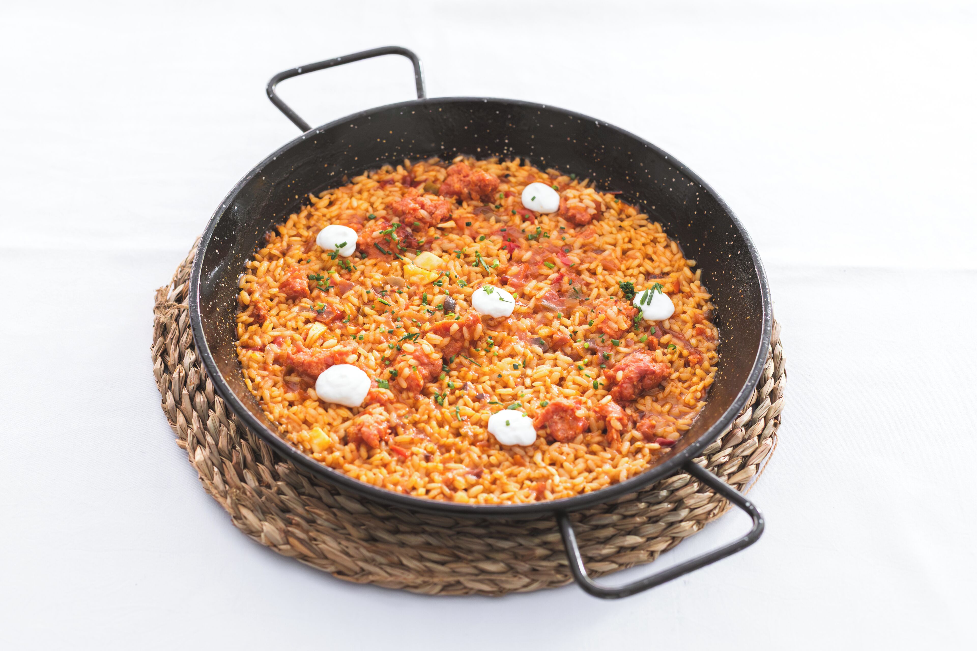 A large, round, black pan filled with rice, tomatoes, and garnished with herbs and dollops of cream.