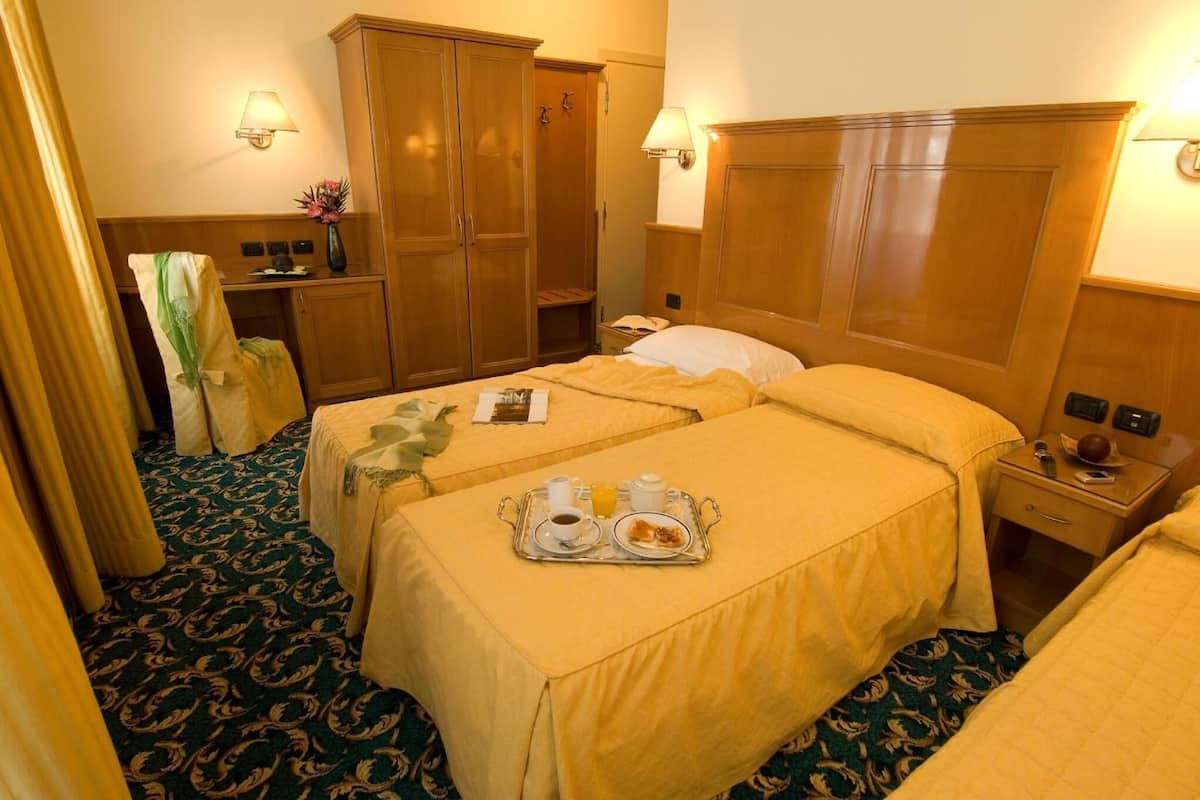 A hotel room with two beds, a wardrobe, a vanity with a mirror, and a tray with breakfast items.
