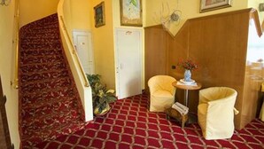 A room with a red carpet, a staircase with a patterned carpet, a white door, two yellow armchairs, a small table with a vase, and a wall-mounted decoration. - Cinque Giornate (Milan)