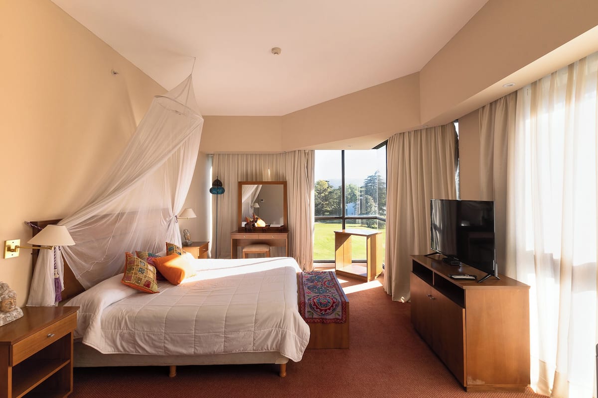 A hotel room with a bed, a TV, a desk, and a balcony with a view.