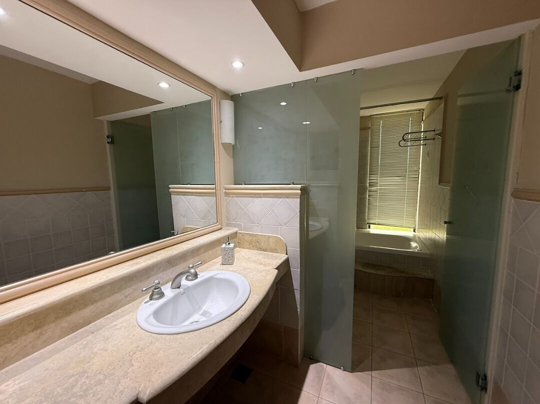 Baño con lavamanos, espejo y zona de ducha.