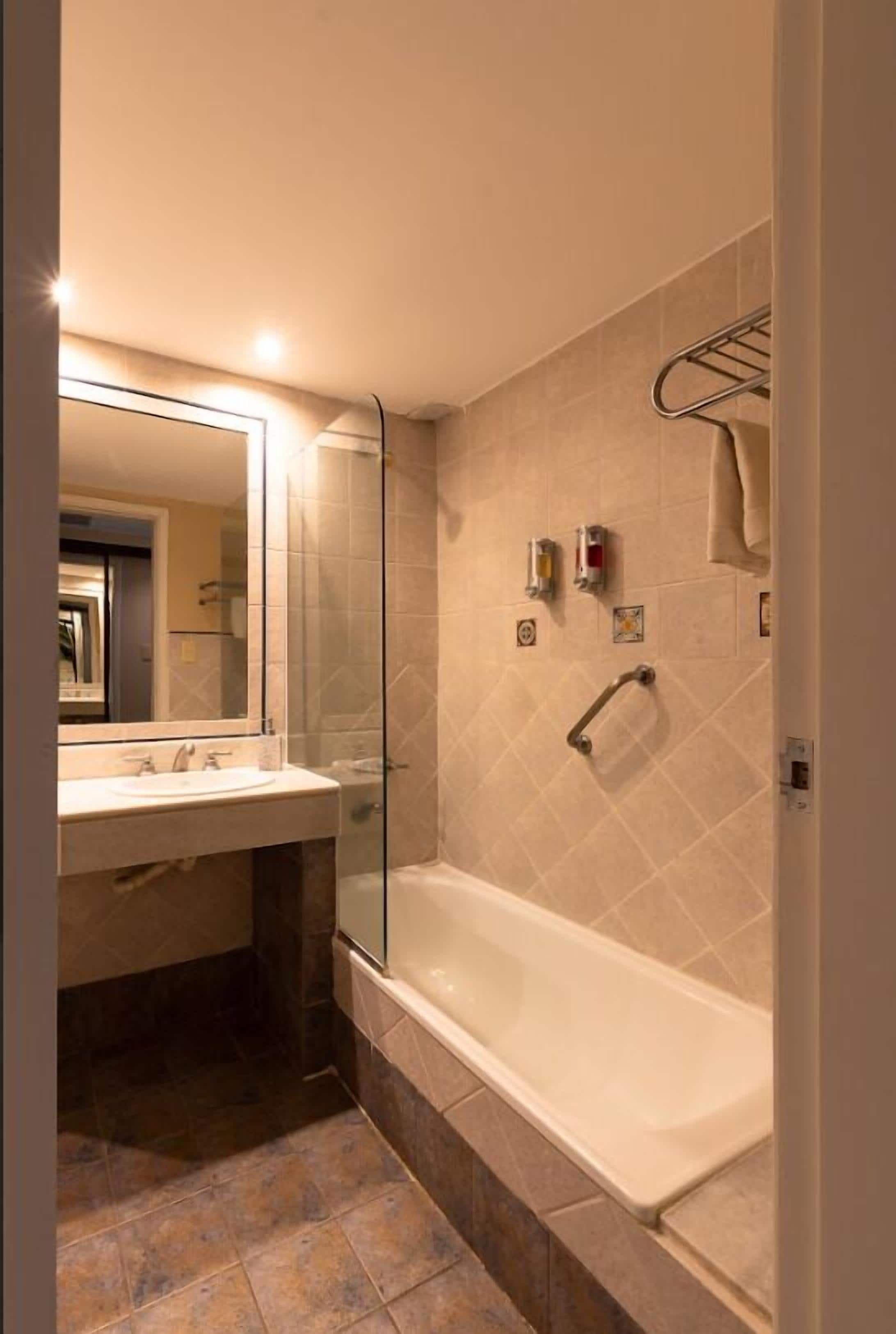 A bathroom with a glass-enclosed shower, a bathtub, a sink, and a mirror.