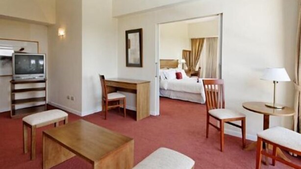 Una habitación de hotel con cama, escritorio, sillas, televisor y lámpara.