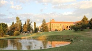 Un campo de golf con un estanque, árboles y un edificio con ventanales arqueados.