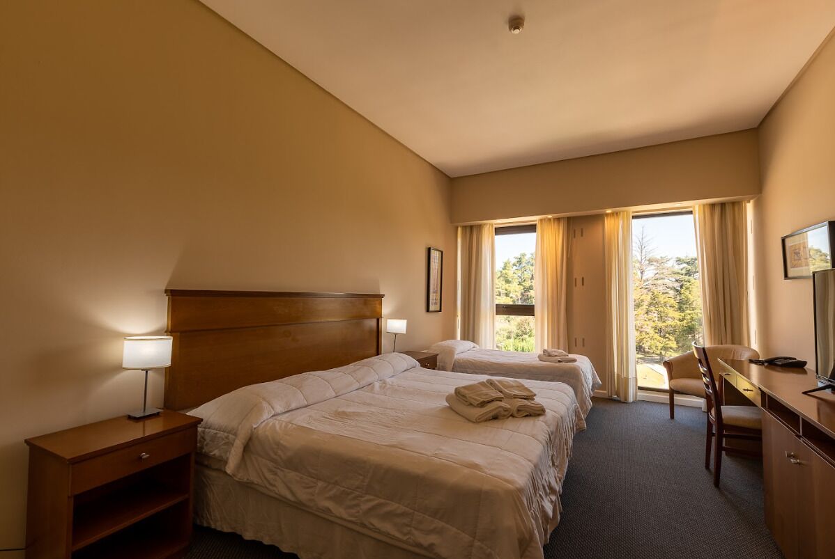 A hotel room with two beds, a desk, a chair, and a window with curtains.