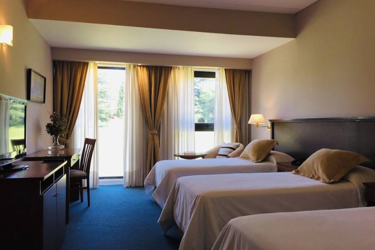 A hotel room with two beds, a desk, a chair, and a window with curtains.