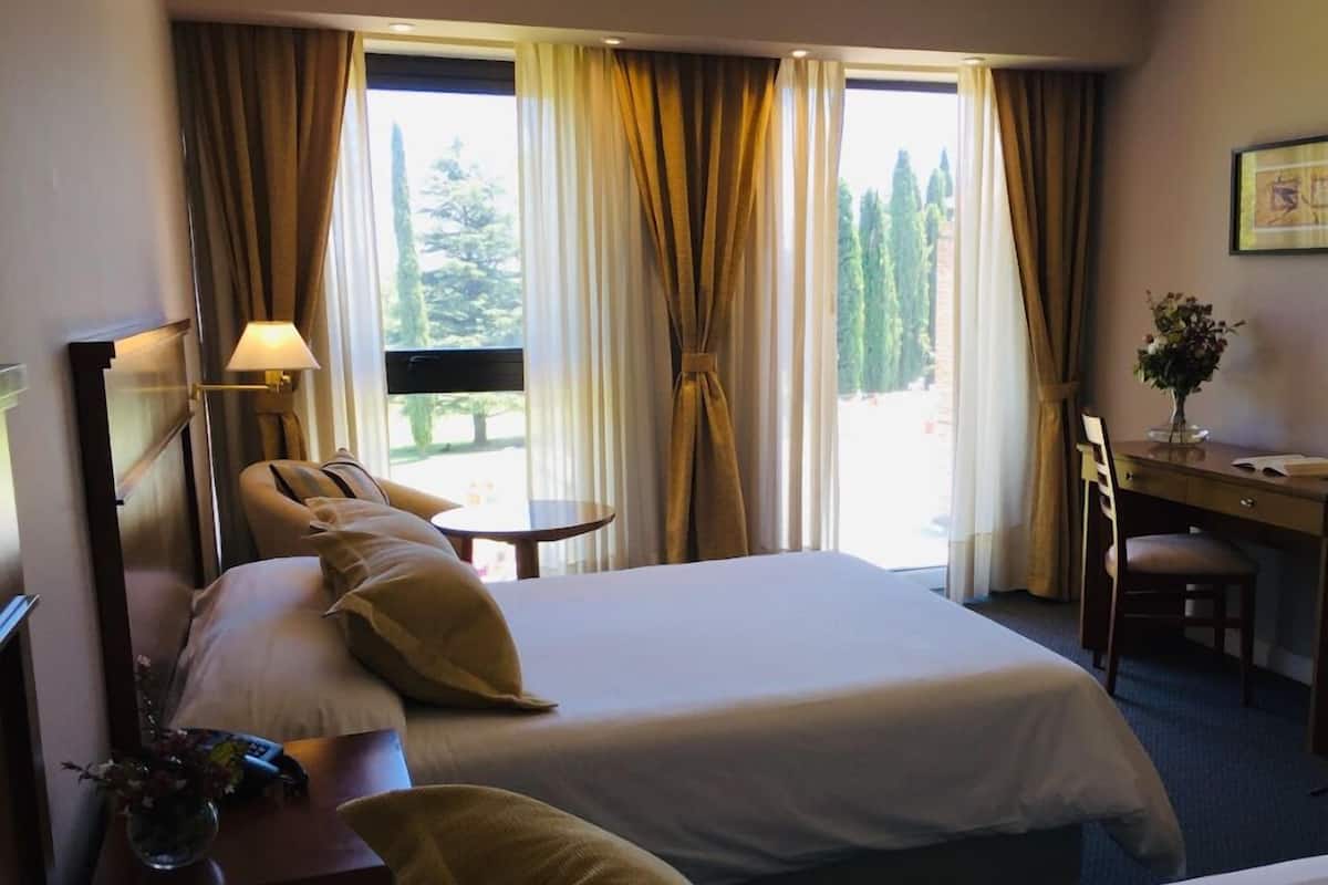 A hotel room with two beds, a desk, a chair, a lamp, and a window with curtains.