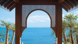Ein hölzerner Pavillon mit bogenförmigem Eingang, der auf ein klares, blaues Meer blickt.
