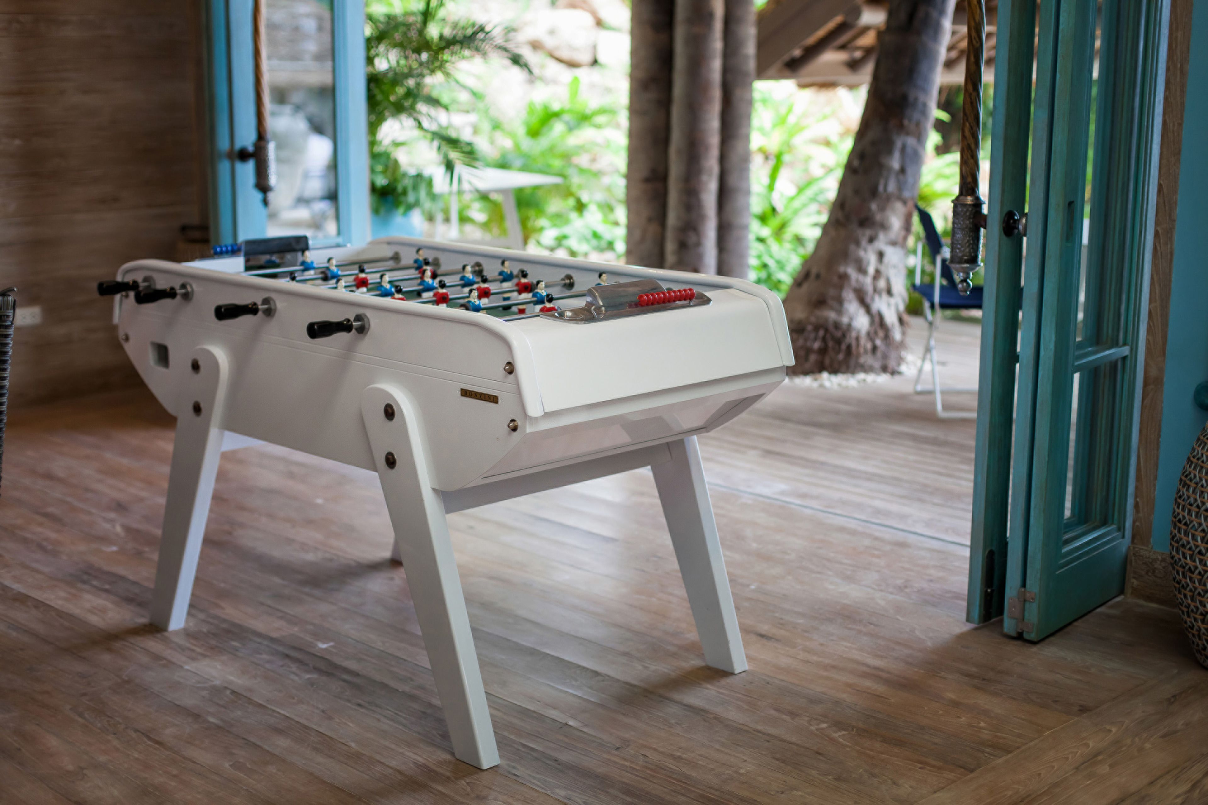 A white foosball table in a room with wooden flooring and a door leading outside.