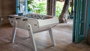A white foosball table in a room with wooden flooring and a door leading outside.
