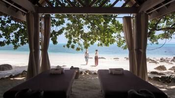 Een strandresort met twee massagetafels, een houten pergola en uitzicht op de oceaan.