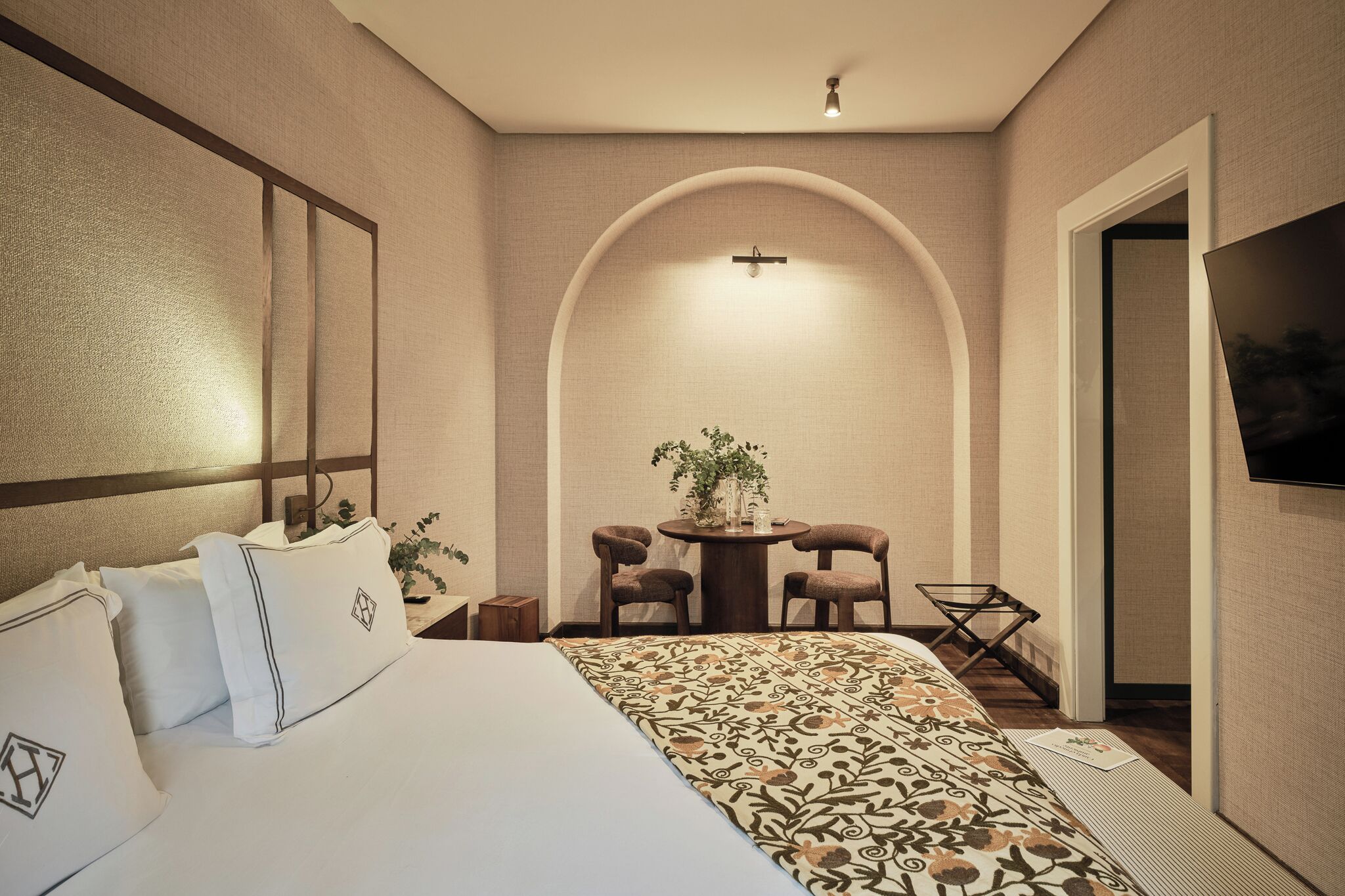 Une chambre d’hôtel avec un grand lit, une petite table avec des chaises, une télévision et une plante.