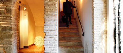 Eine Steintreppe mit einer Person, die hinabgeht, gesäumt von tonbogigen Ziegelmauern und einer kugelförmigen Leuchte am unteren Ende.