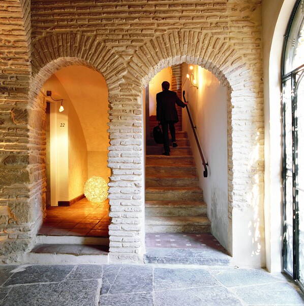 A stone staircase with a person descending, flanked by arched brick walls and a spherical light fixture at the bottom.