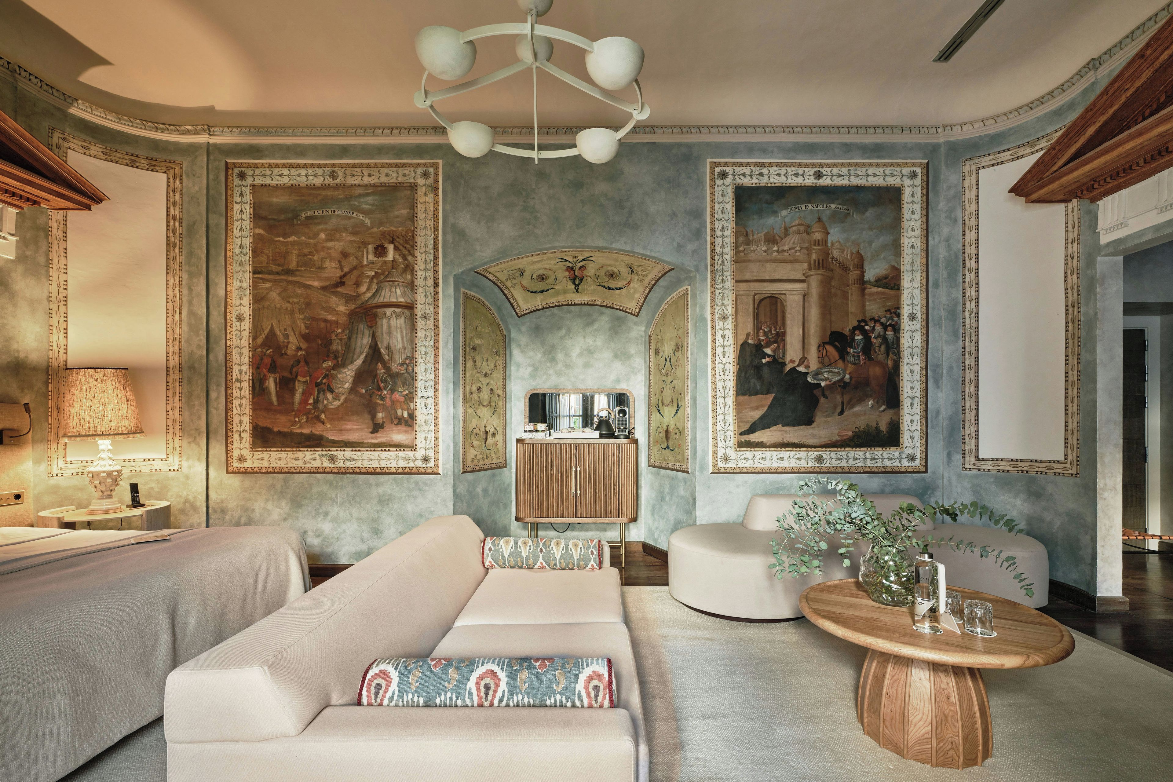 A room with a sofa, a coffee table, and a cabinet. There are paintings on the walls.