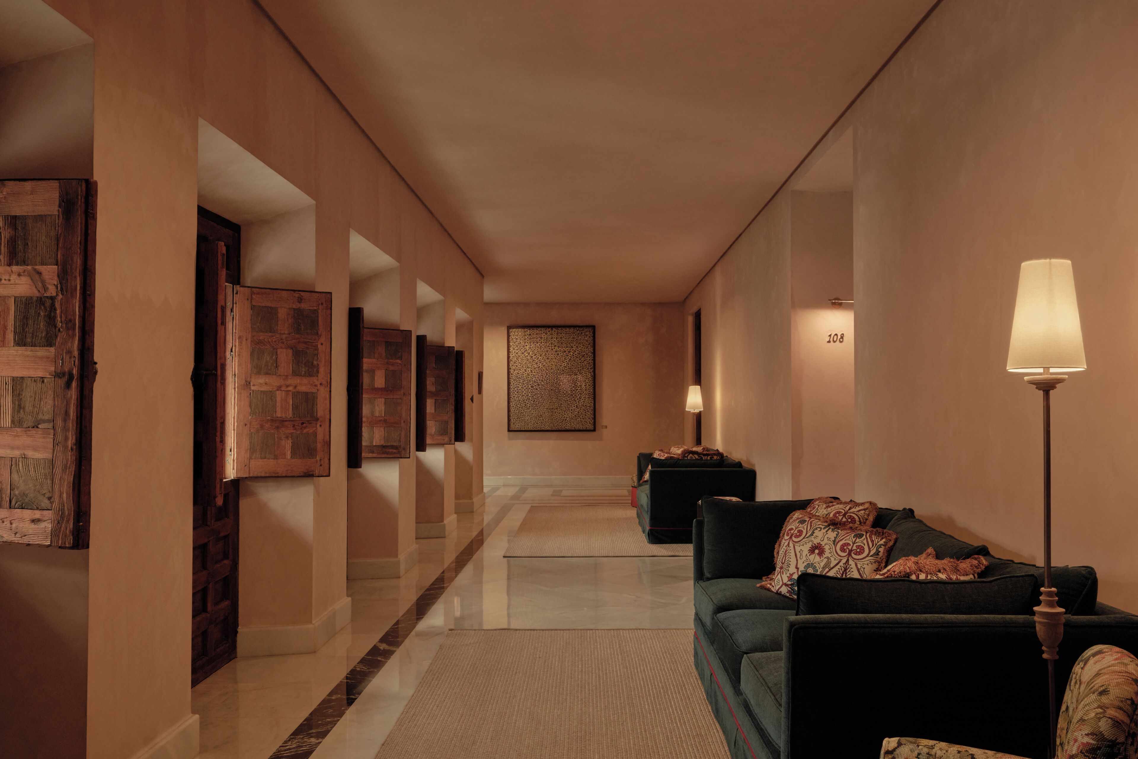 A corridor with a sofa set, wall-mounted lamps, and framed artwork.