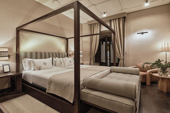 Una cama con dosel sostenido por cuatro postes, con estructura de madera, un espejo grande y una mesita de noche con lámpara.