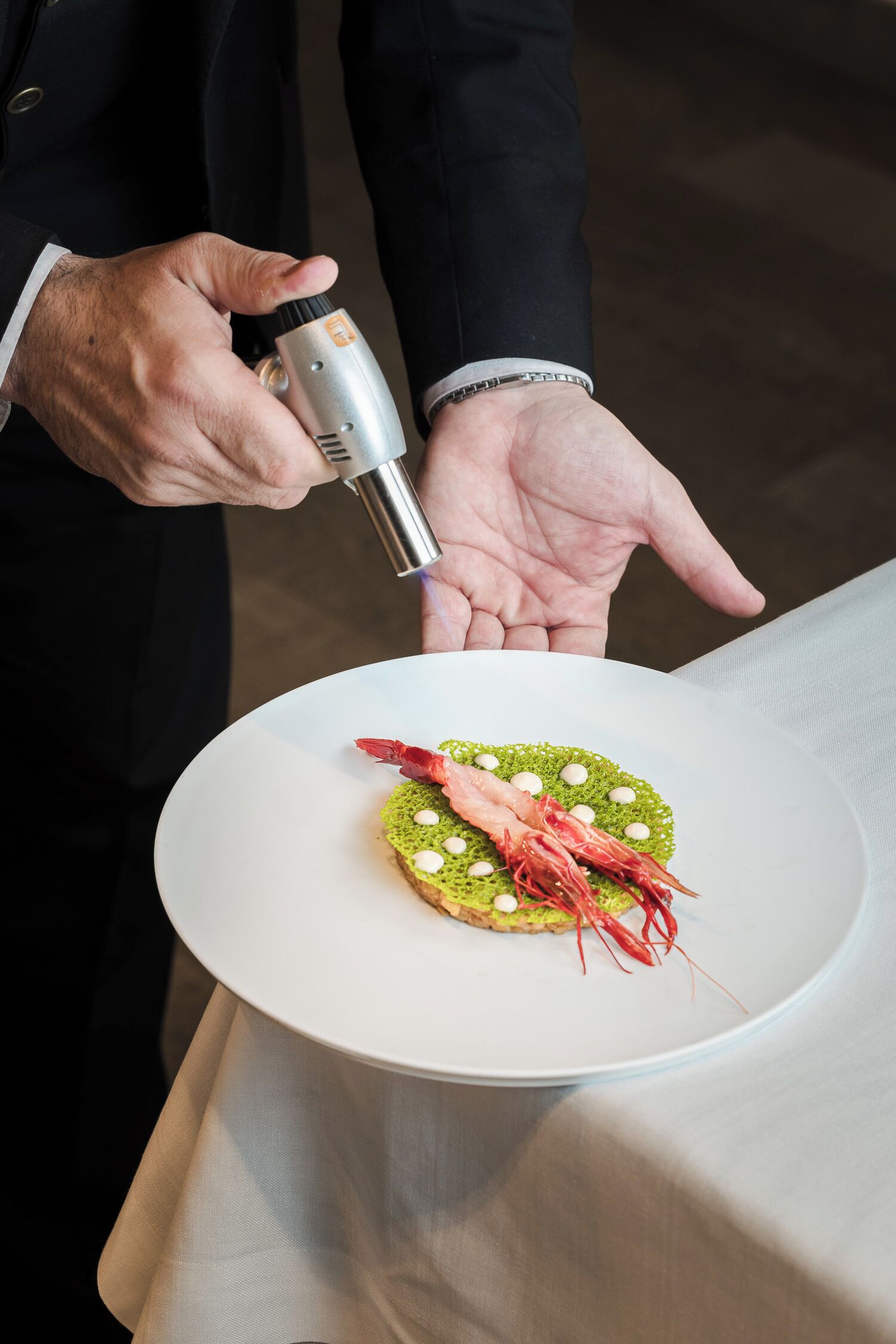 Una persona sosteniendo un plato con un guiso que lleva camarones y guarnición verde.