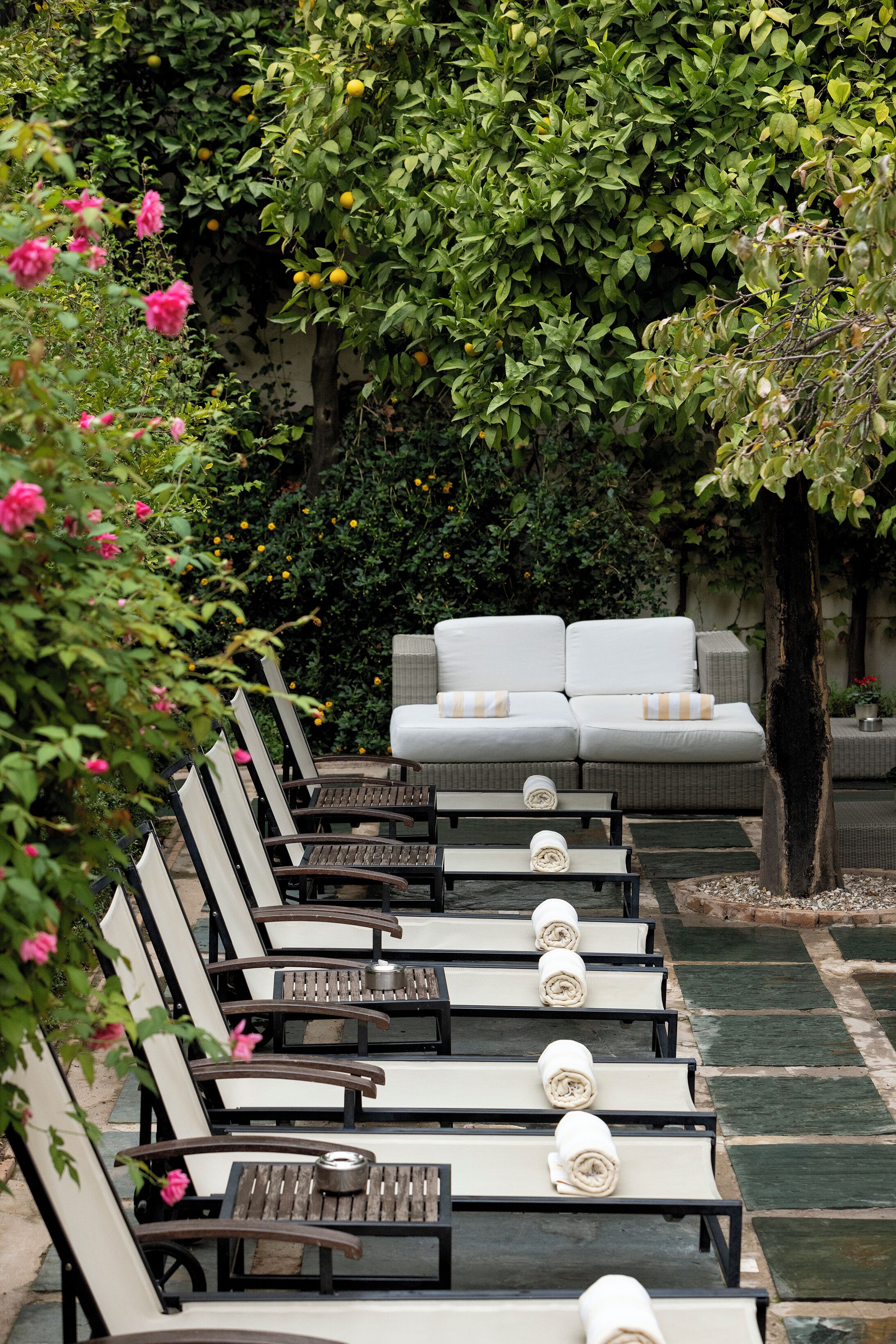 Un conjunto de sillones de descanso con toallas, un sofá blanco y un exuberante jardín de fondo.
