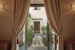 Una entrada con cortinas color beige, un sendero de piedra, una puerta y una pequeña fuente.
