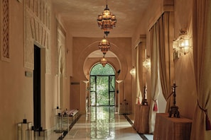 A hallway with a glass door leading to a green outdoor area, ornate wall decorations, and hanging lanterns.