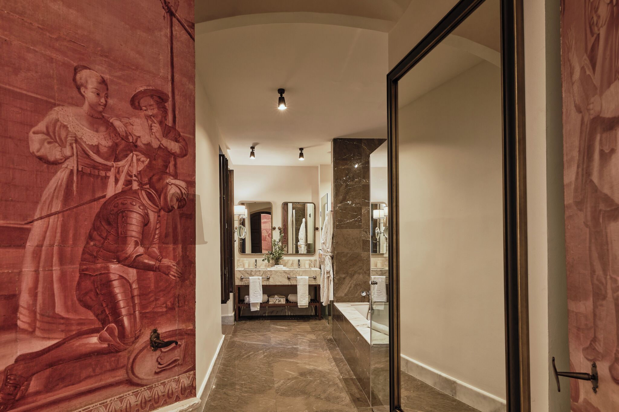 A hallway with a marble floor, a large mirror, and a modern bathroom with a bathtub and vanity.