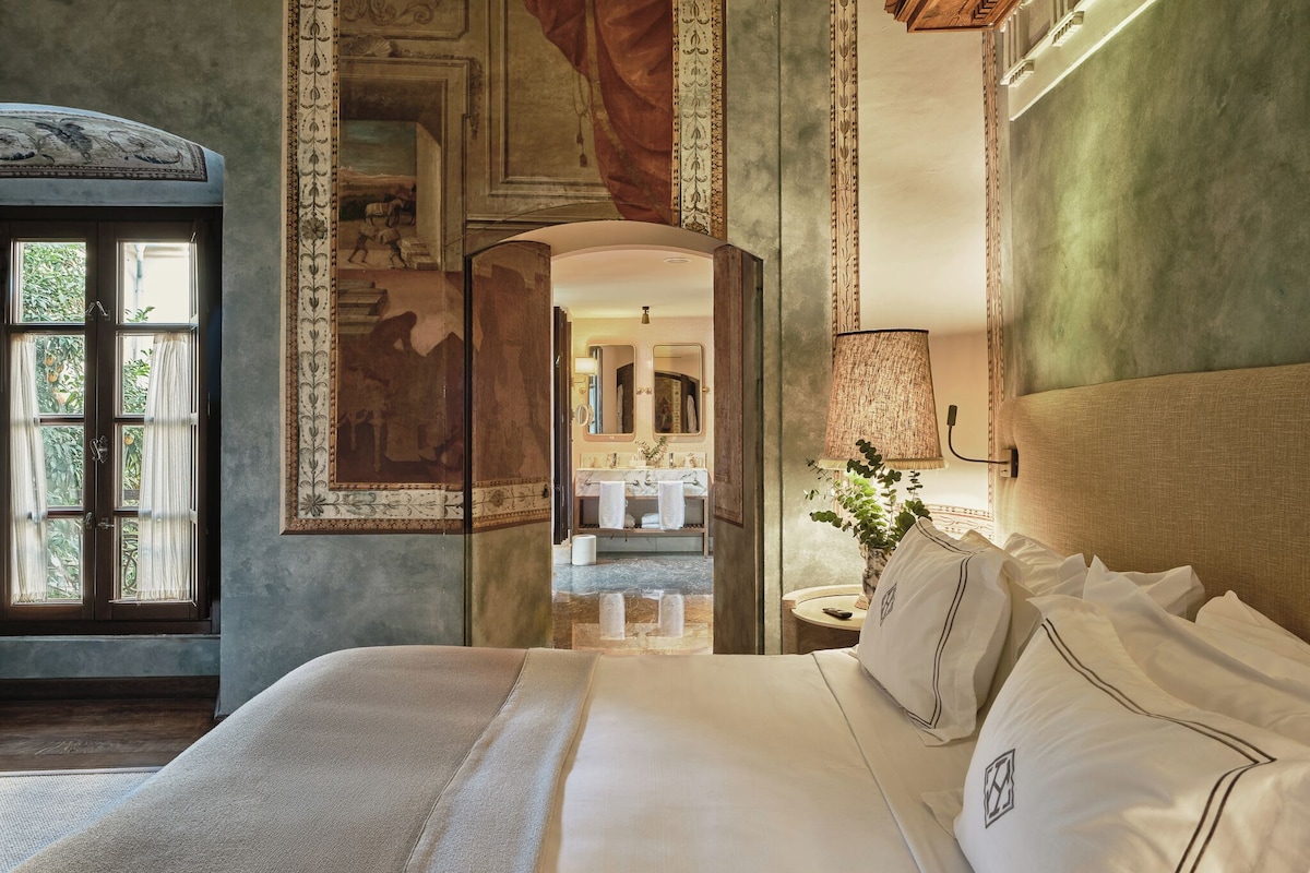 A spacious bedroom with a large bed, a view of the bathroom, and a decorative ceiling.
