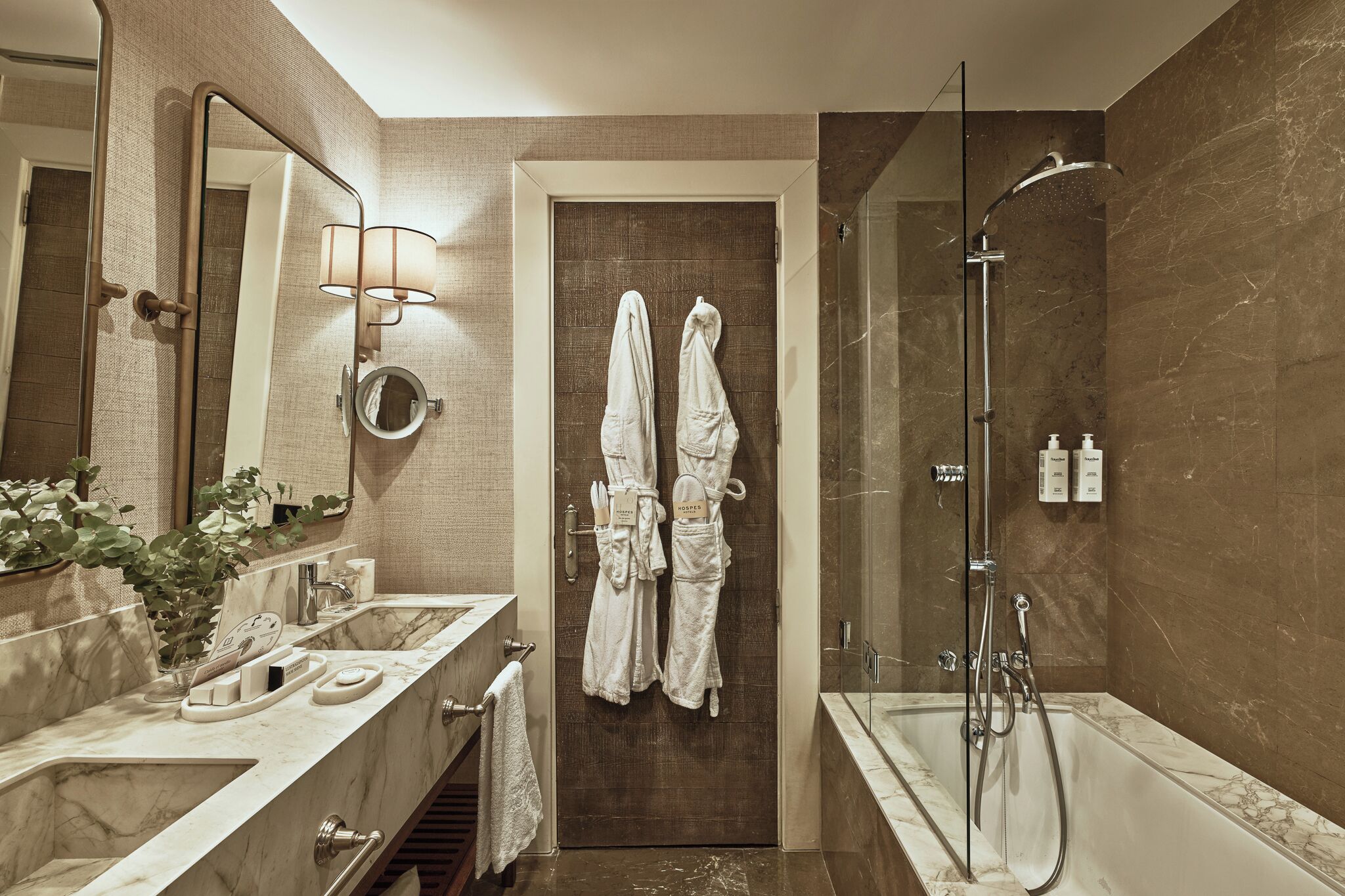 A modern bathroom with a marble sink, a large mirror, a shower, and two towels hanging on the door.