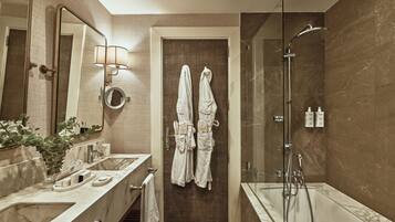 A modern bathroom with a marble sink, a large mirror, a shower, and two towels hanging on the door.