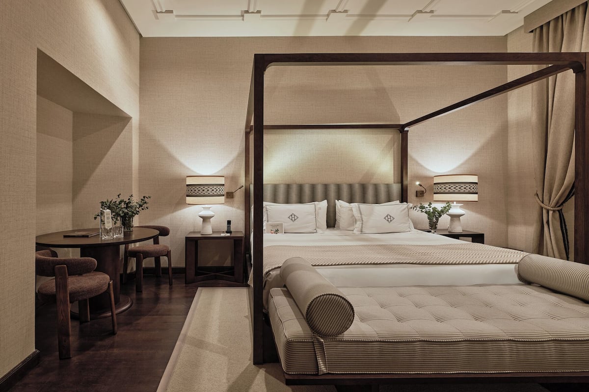 A four-poster bed with a canopy, a round dining table with chairs, a small side table, and a lamp.