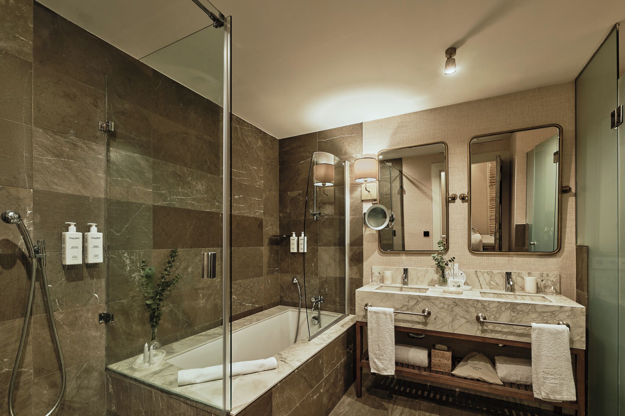 Un baño moderno con ducha de vidrio, tocador de mármol y un espejo grande.