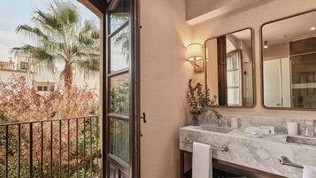 Un baño con lavamanos de mármol, un espejo grande y vistas a una palmera afuera.